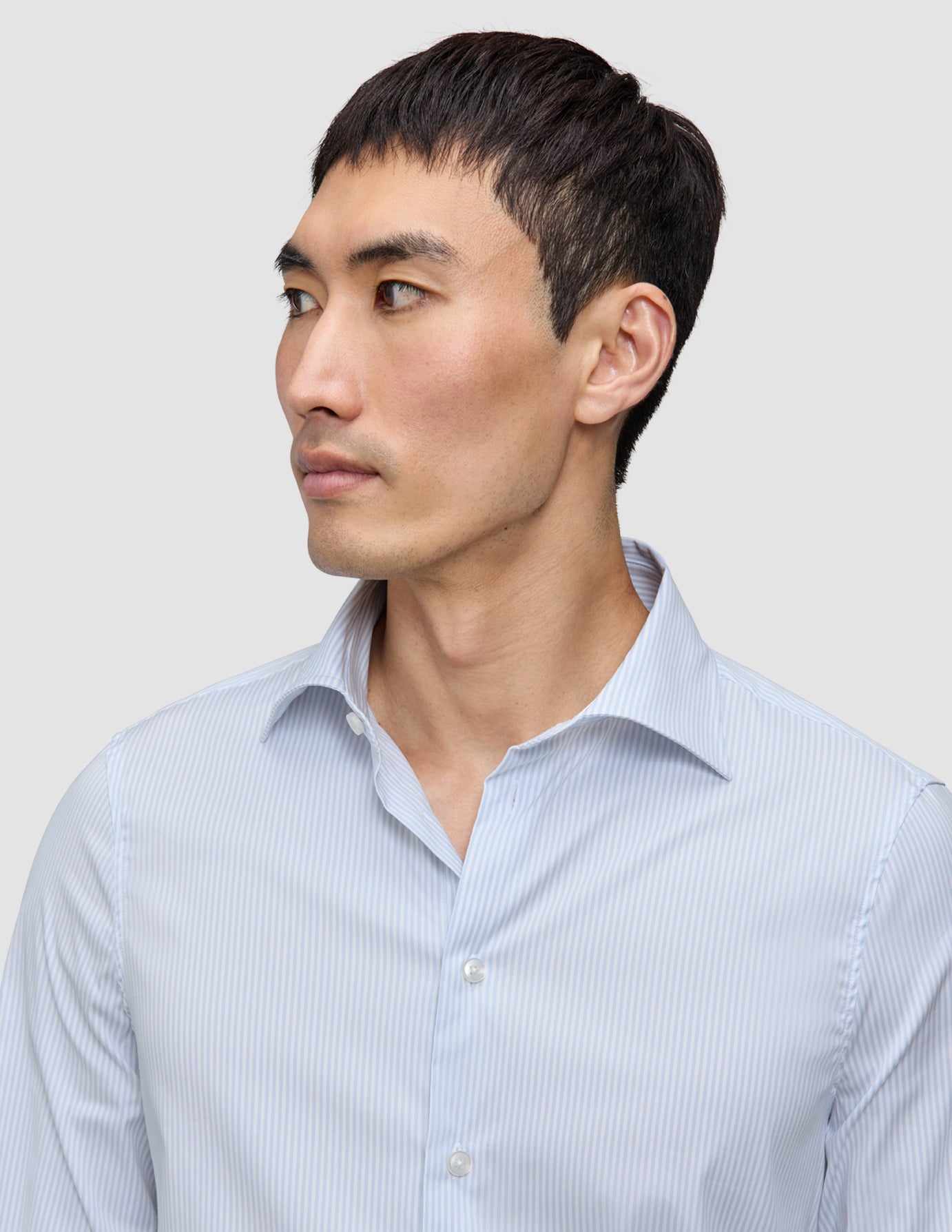 Mann iført en Elevated Shirt Regular Classic Blue Striped – en lysblå og hvit Pima-bomullsskjorte med knapper og tynne striper.